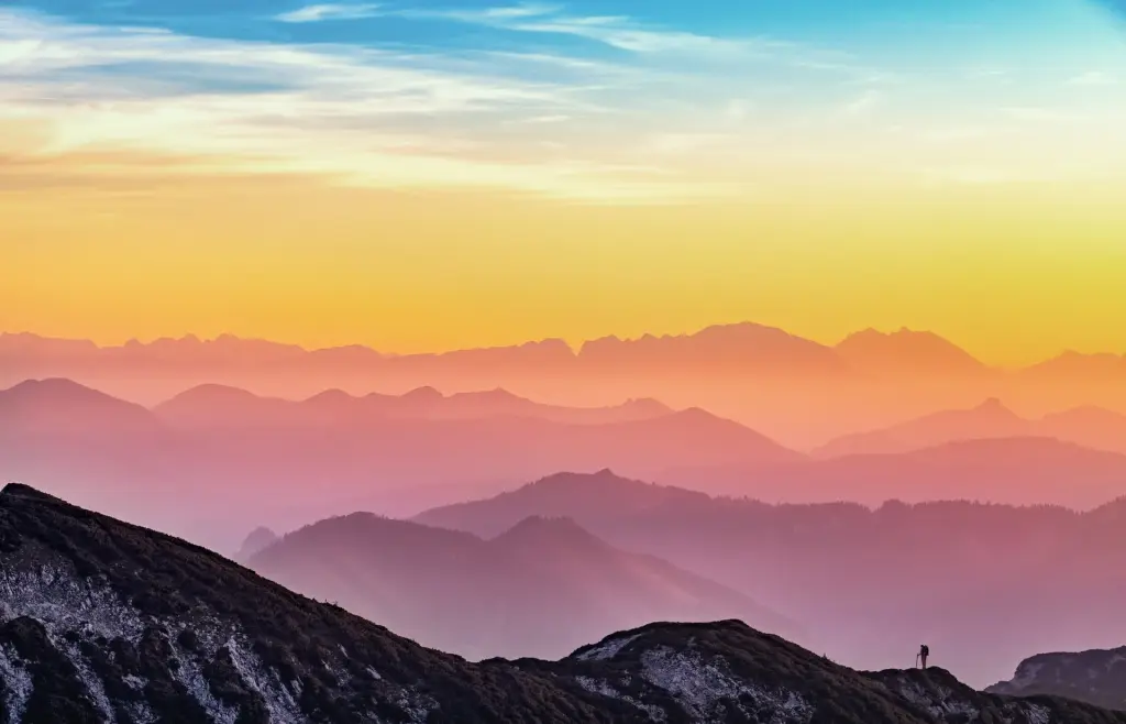Mountains showing on the horizon with a pink, orange and blue sky above. One hiker is standing alone on the right.